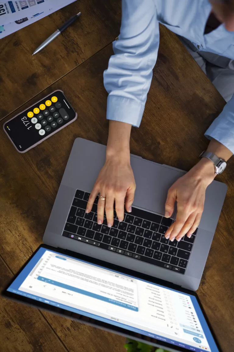 Profissional digitando em laptop com calculadora aberta no celular e documentos à mesa, simbolizando a análise estratégica de custos com apoio da TI.