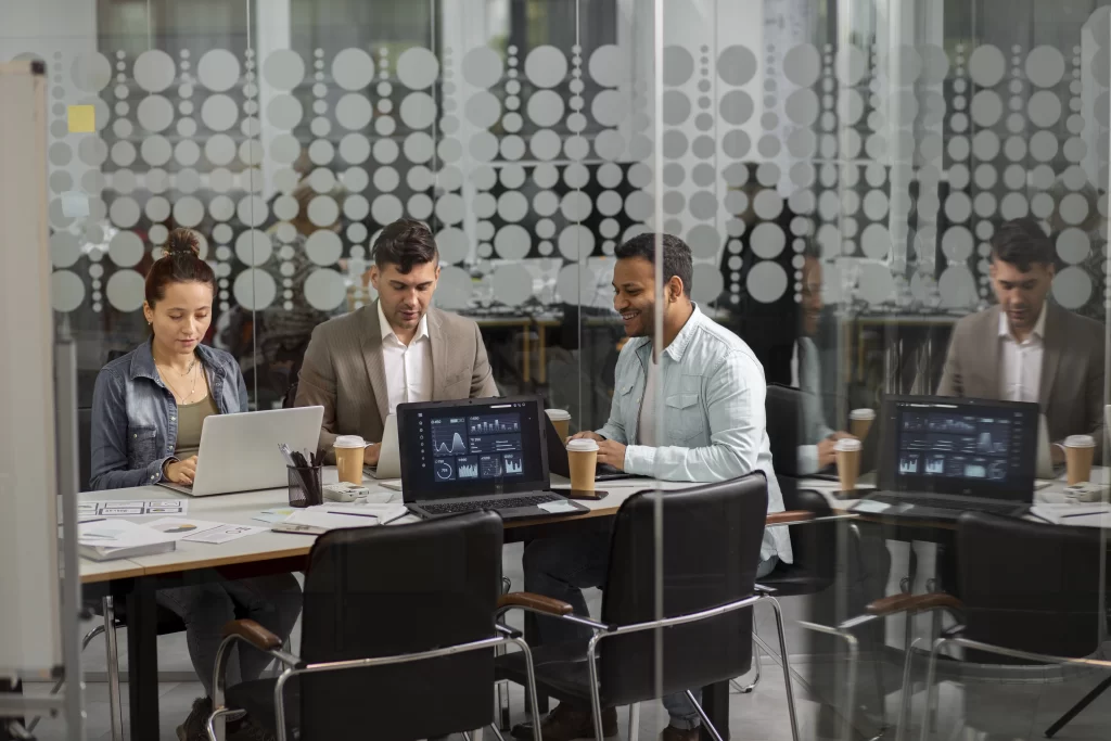 Profissionais reunidos em uma sala de vidro analisando dashboards de dados em notebooks, representando a atuação estratégica do outsourcing de TI na performance das empresas.