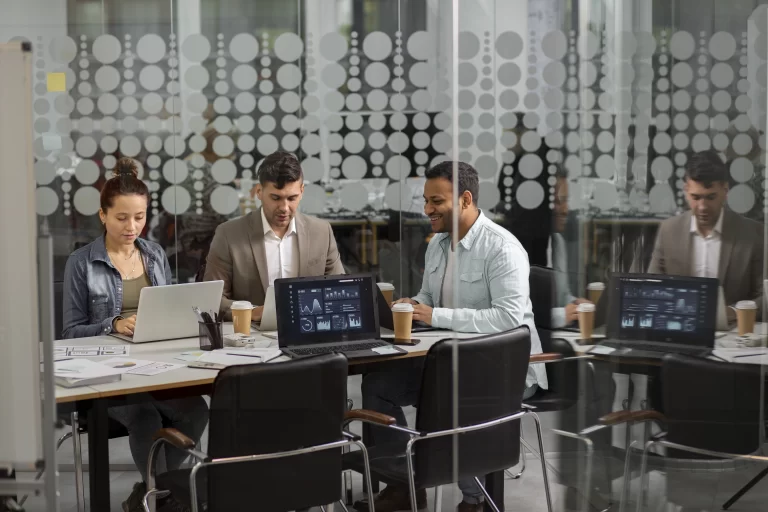 Profissionais reunidos em uma sala de vidro analisando dashboards de dados em notebooks, representando a atuação estratégica do outsourcing de TI na performance das empresas.
